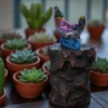Colorful handcrafted clay Krishna idol on a crescent moon, placed on a rock-like base surrounded by green potted succulents — terracotta home decor sculpture.