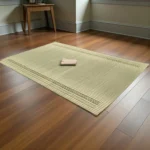Handmade natural reed grass mat placed on a wooden floor with a folded cloth on top – eco-friendly Madurkathi sleeping and yoga mat.