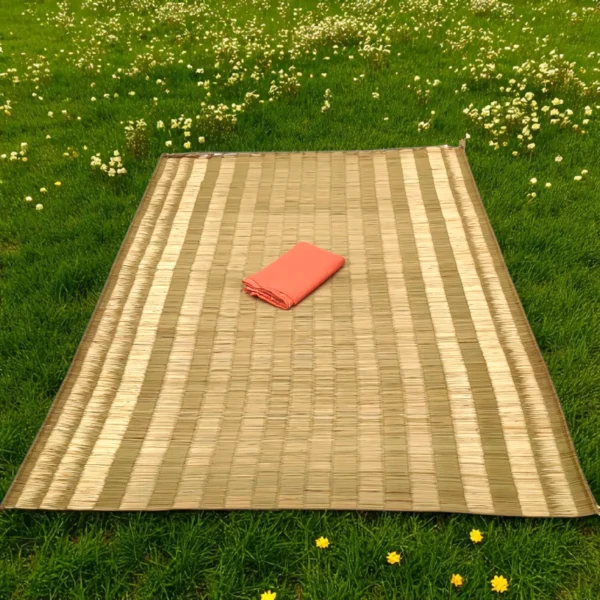 Handwoven Korai Grass Mat placed on green grass outdoors with a folded orange cloth on top