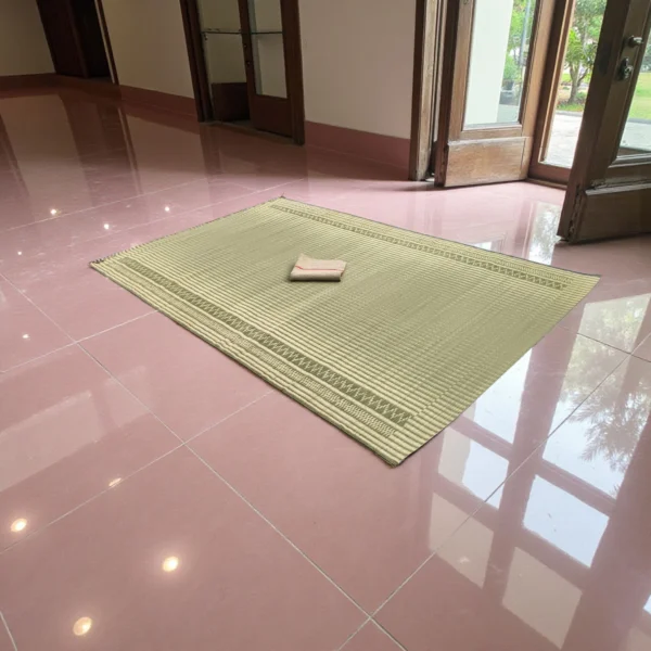 Handwoven natural reed grass (Madurkathi) mat placed on a glossy tiled floor near open wooden doors – eco-friendly sleeping and yoga mat.