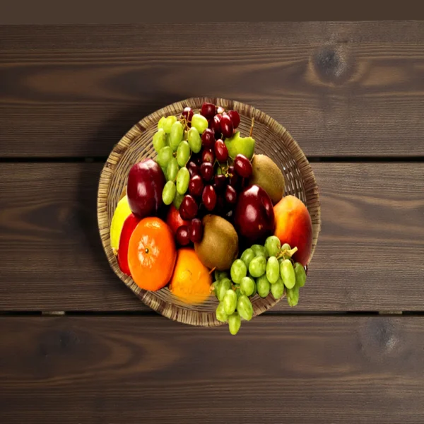 Handwoven bamboo basket filled with fresh fruits like apples, oranges, grapes, and kiwi on a wooden table.
