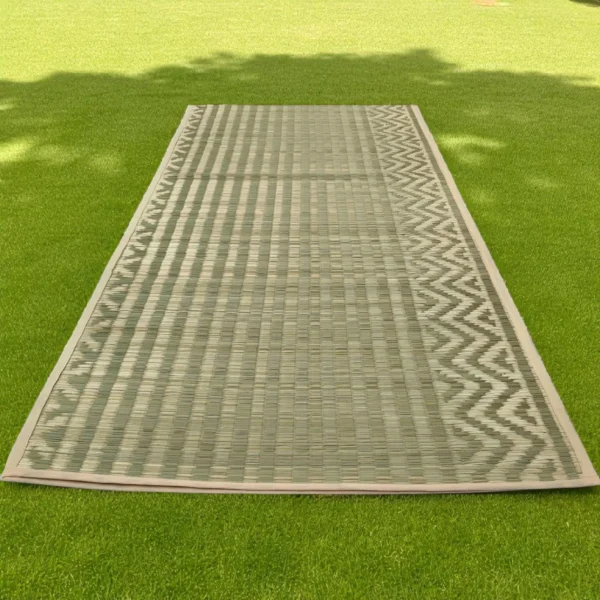 Handwoven natural Madurkathi grass mat placed in a cozy living room with wooden flooring.