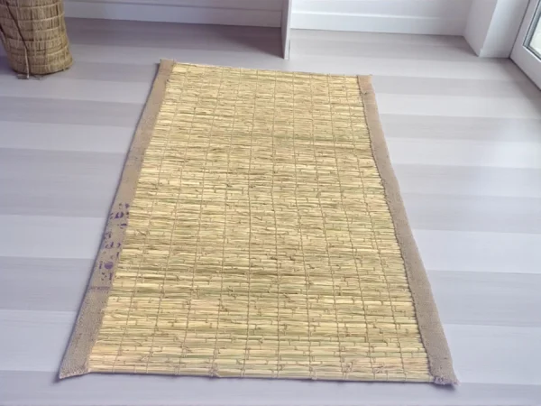 Natural handwoven Kusha grass mat placed indoors on a tiled floor near wicker chairs and potted plants – eco-friendly mat for puja, yoga, and meditation.