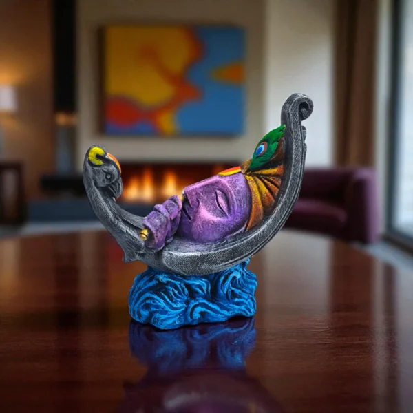 Handcrafted colorful terracotta Krishna idol resting on a crescent moon, playing flute, displayed on a wooden table with a warm home interior background.