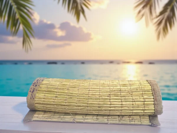 Natural handwoven Kusha grass mat rolled on a wooden surface with sea and sunset in the background — eco-friendly yoga and meditation mat.