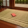 Handwoven Korai Grass Mat placed on wooden floor near window with a folded cloth on top