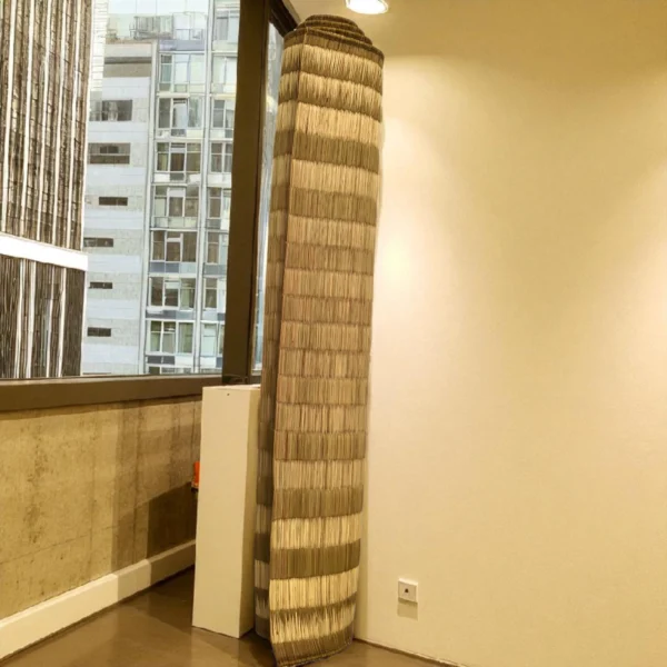 Rolled handwoven Korai Grass Mat standing upright in a modern room near a window