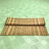 Folded handwoven Korai Grass Mat placed on a light green tiled floor