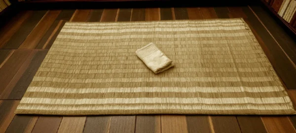 Handwoven Korai Grass Mat placed on a wooden floor with a folded cloth on top
