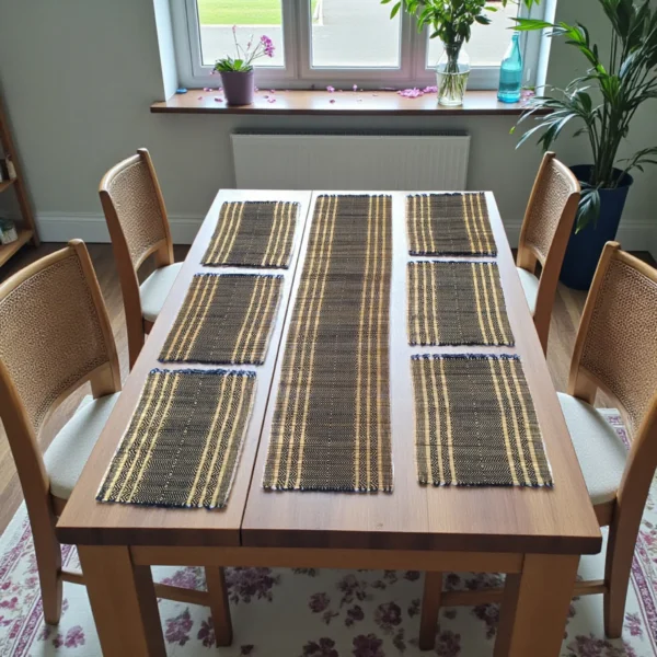 Handwoven black and natural-striped grass table mats with a matching long table runner arranged neatly on a wooden dining table in a bright dining room.