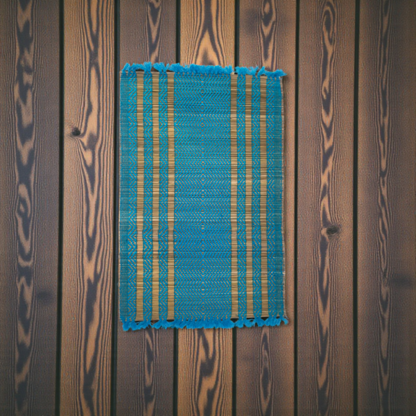 Handwoven blue and natural-striped grass table mat with fringe edges displayed on a wooden textured background.