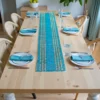 Handwoven blue and natural-striped table runner placed on a wooden dining table set with plates, napkins, and glasses in a bright modern dining room.