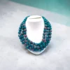 Handmade teal floral fabric bead multi-layer necklace displayed on white stand minimal background