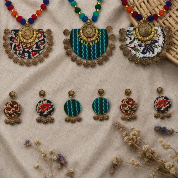 Handmade terracotta jewelry sets with floral and striped fabric pendants and matching earrings displayed on neutral linen background with dried flowers