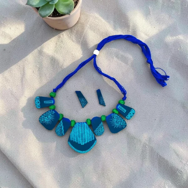 Handmade blue tribal fabric necklace set with matching earrings placed on beige fabric background, boho statement jewelry flat lay