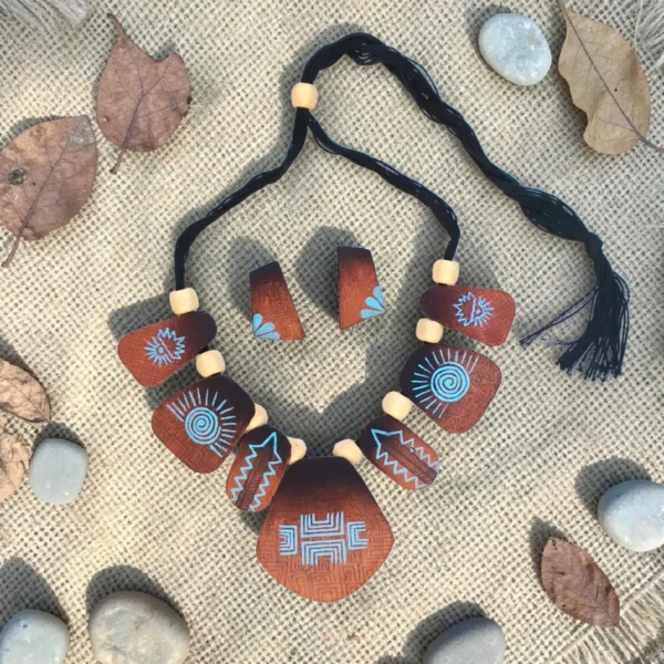 Handmade brown tribal fabric necklace set with matching earrings on textured fabric with leaves and stones, boho statement jewelry flat lay