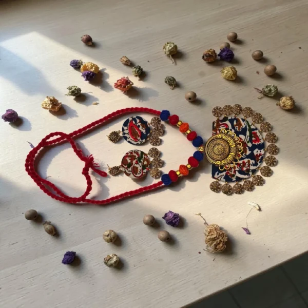 Handmade terracotta necklace set with floral fabric pendant and matching earrings, styled with red thread beads on wooden surface with dried flowers