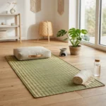 Handmade eco-friendly natural reed grass yoga and meditation mat placed on a wooden floor with a meditation cushion, towel, water bottle, and indoor plants in a bright, minimalist home.