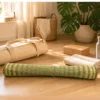 Rolled handmade natural reed grass yoga and meditation mat on a wooden floor with a yoga bag, cork block, towel, and water bottle, highlighting its lightweight, portable, eco-friendly design.