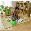 Young child studying on a handmade natural reed grass mat in a bright home library with books, notebooks, colored pencils, and wooden bookshelves, showcasing an eco-friendly Korai grass floor mat.