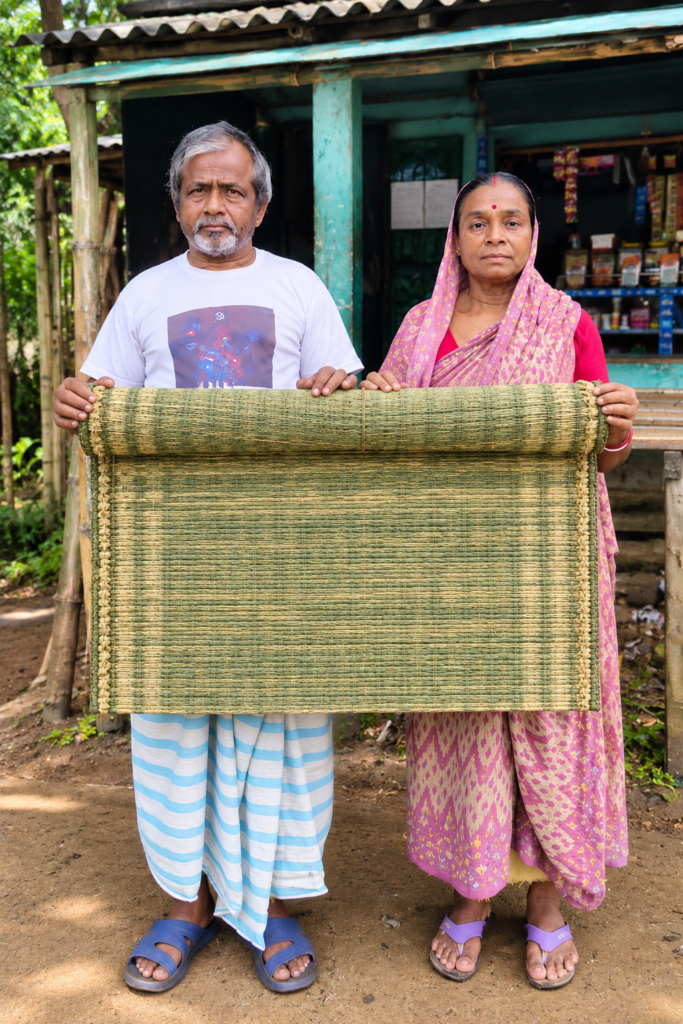 রাজপুর–আরগোড়ার কারিগর মণীন্দ্র বেরা ও কৌশল্যা বেরা হাতে তৈরি প্রাকৃতিক মাদুর নিয়ে দাঁড়িয়ে আছেন