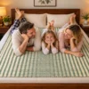 “Handmade natural grass mat with a green and cream striped woven design spread across a wooden bed, with a smiling family of three relaxing together in a warm and cozy bedroom.”